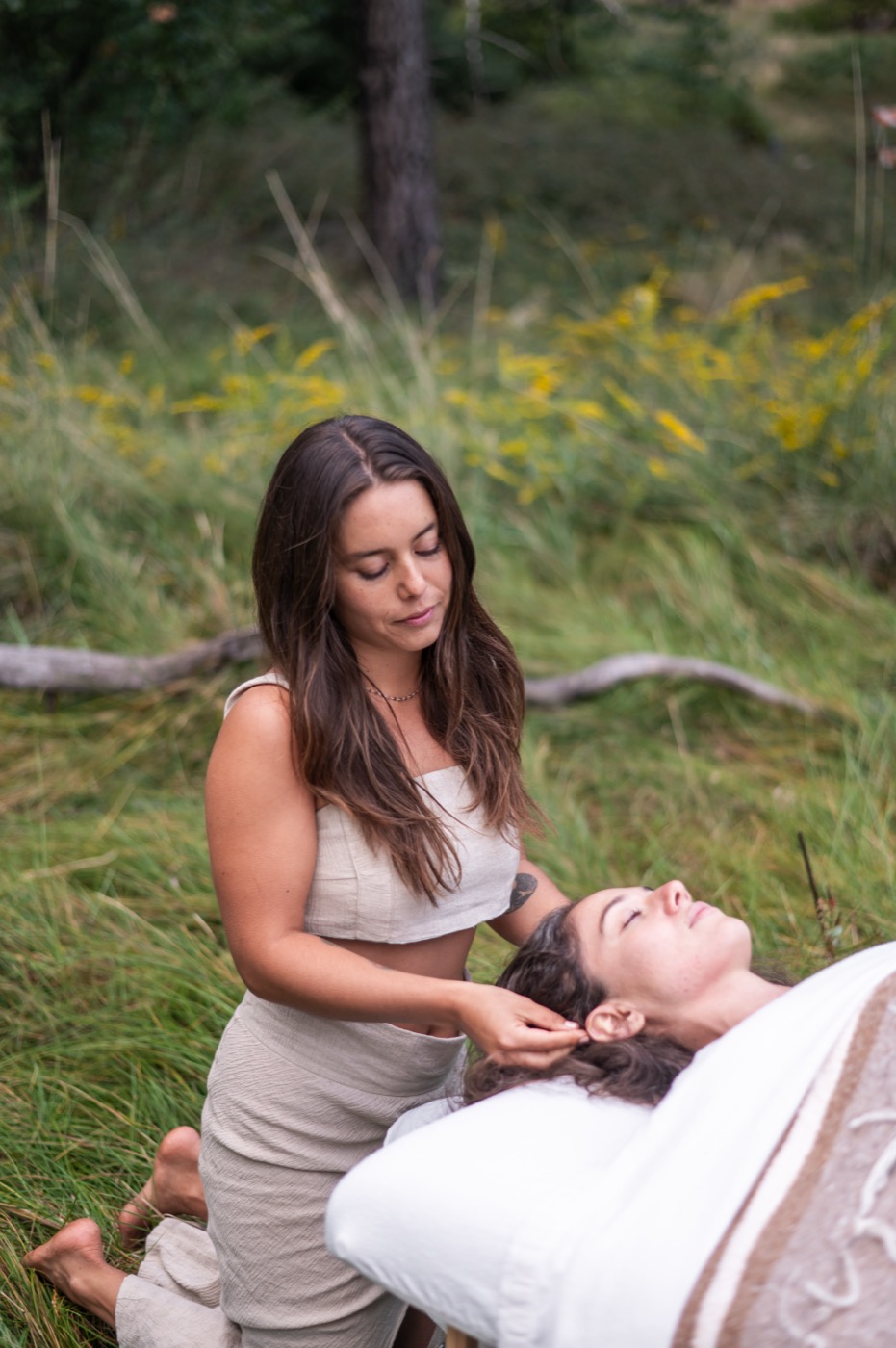 Katrinna Jasso performing cranial massage outdoors in a forest meadow with golden wildflowers